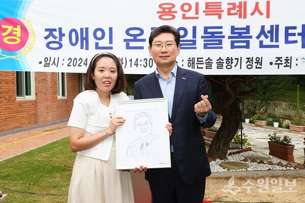 1일 개소한 ‘용인시 장애인온종일돌봄센터’에서 이상일 용인시장(오른쪽)이 시장 얼굴을 직접 그린 캐리커쳐를 선물한 발달장애인 화가 이미경 작가와 기념촬영을 하고 있다. (사진=용인시)