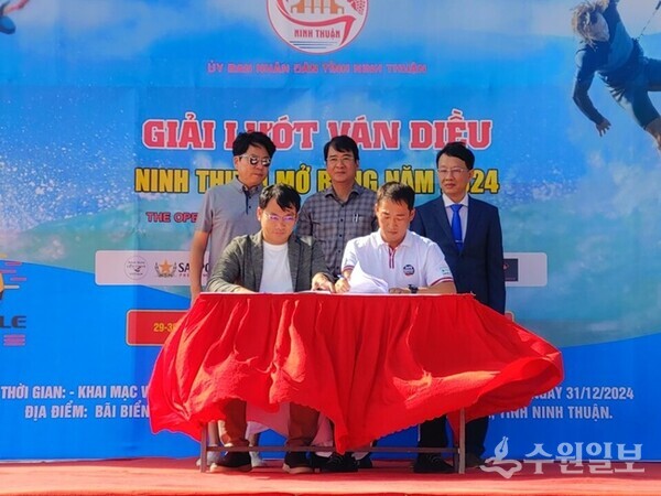 1. 베트남 닌투언성 미호아(My Hoa) 해변에서 30일 열린 ‘2024 닌투언 국제카이트서핑대회’ 개회식에서 대한민국 ‘제주국제슈퍼컵카이트보딩대회’와 베트남 ‘닌투언 국제카이트서핑대회’가 양국의 해양스포츠 발전과 관광 교류 협력을 약속하는 양해각서를 체결했다. 박성제 제주특별자치도 해양레포츠협회장(앞줄 오른쪽)과 응우옌 안 부 닌투언관광협회장(앞줄 왼쪽)이 상호 협력을 약속하는 양해각서에 서명하고 있다. 뒷줄 오른쪽부터 닌투언 국제카이트서핑대회 응우옌 반 호아(Nguyen Van Hoa) 조직위원장(닌투언성 문화체육관광부 국장), 응우옌 롱 비엔(Nguyen Long Bien) 닌투언성인민위원회 부위원장, 제주국제슈퍼컵카이트보딩대회 공동주관 제주의소리 김봉현 이사 (사진=제주의 소리)