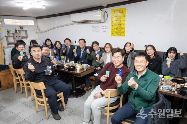 수원시 공직자들이 수원 지역경제 활성화를 위해 골목상권을 이용한 뒤 수원페이를 들어보이고 있다.(사진=수원시)